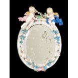 A 19th Century porcelain oval girandole mirror, the body surmounted by a pair of Putti holding a
