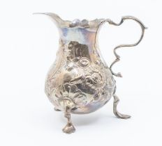 A George II silver baluster cream jug, wavy rim above body later chased with flowers, S scroll