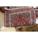 A hand knotted woollen rug, with stylised foliage design on a red ground, blue and cream borders,