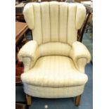 An early 20th century upholstered wingback armchair, cream patterned fabric, raised on square