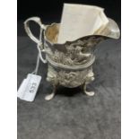 Hallmarked Silver (Irish): Helmet cream jug embossed with country scenes, with a C scroll handle,