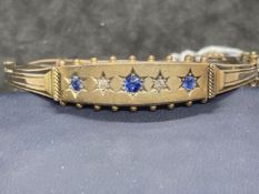 Yellow metal late Victorian bangle set with three sapphires and ten rose cut diamonds, stamped