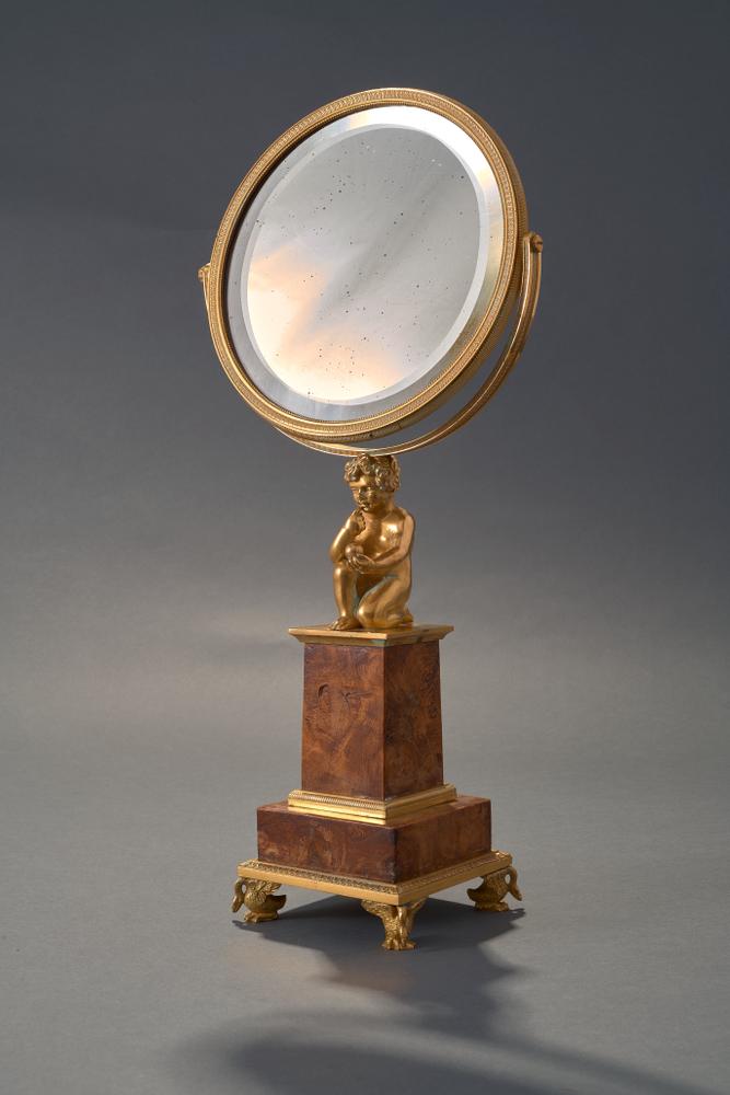 GILDED BRONZE FRAMED MIRRORset on marble column with square base. The mirror is held by a kneeling