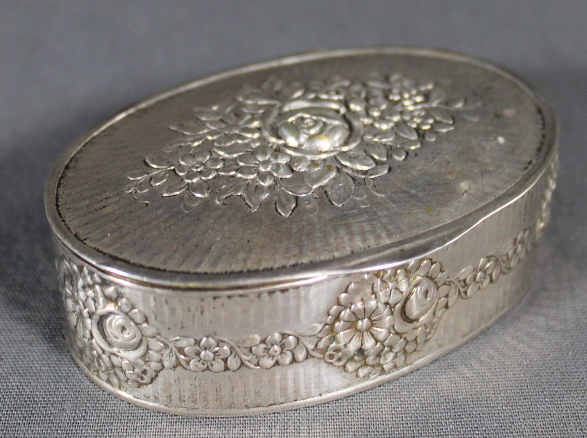 1 ovale Dose Silber (800/000), punziert, Deckel und Wandung mit getriebenem Blumendekor,