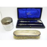 A silver backed brush, a silver topped glass jar, top dented, and a cased shoe horn and button hook