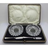 A pair of cut glass butter dishes with two silver butter knives, boxed