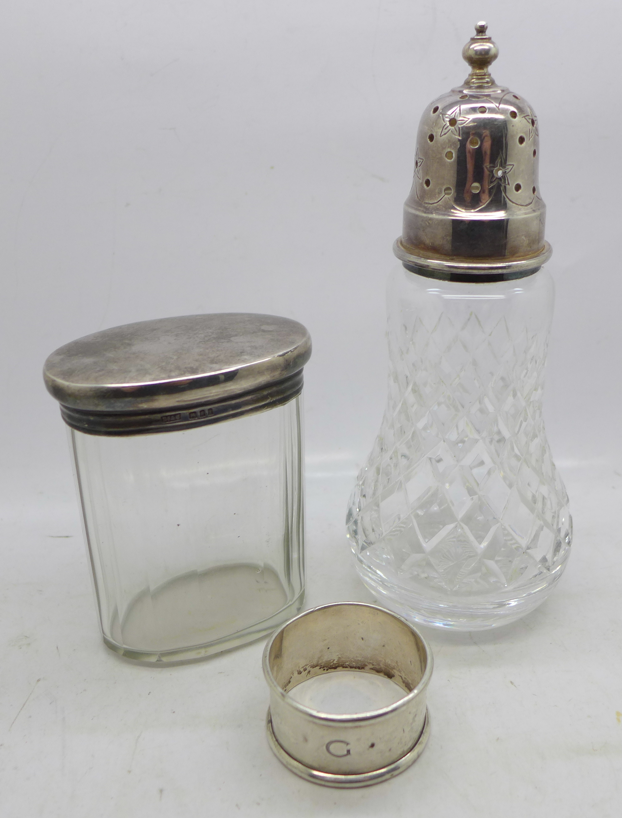 A silver topped sugar castor, a silver topped dressing table jar and a silver napkin ring