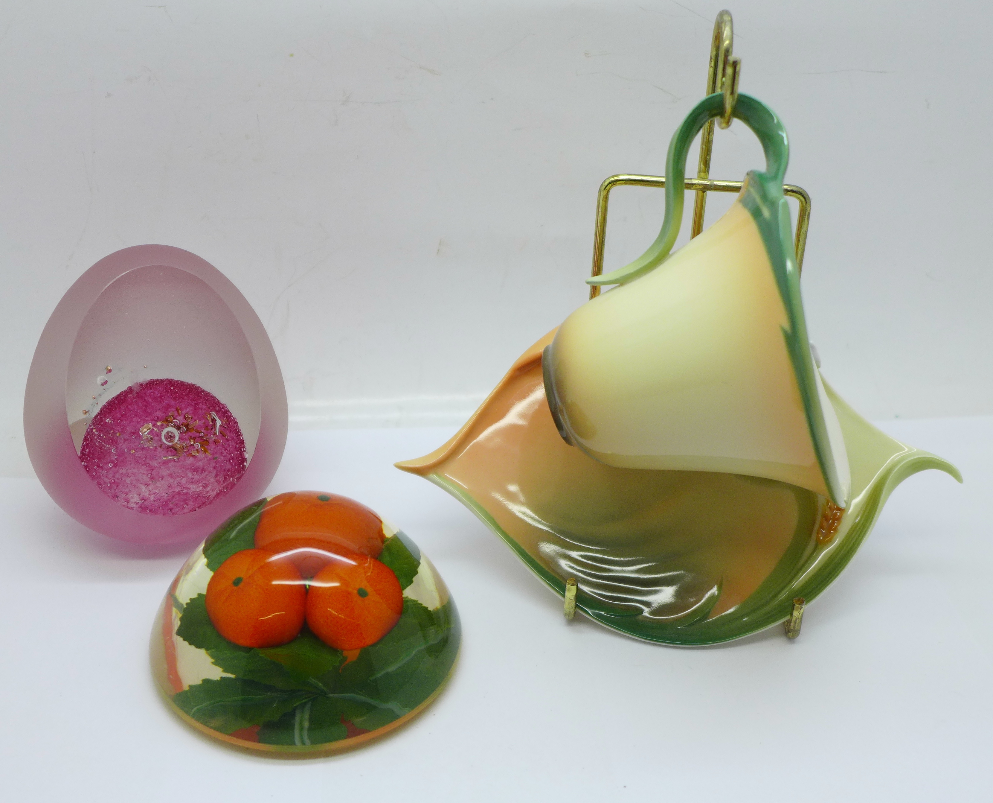 A Franz Porcelain cup and saucer with display stand, a French glass paperweight and one other