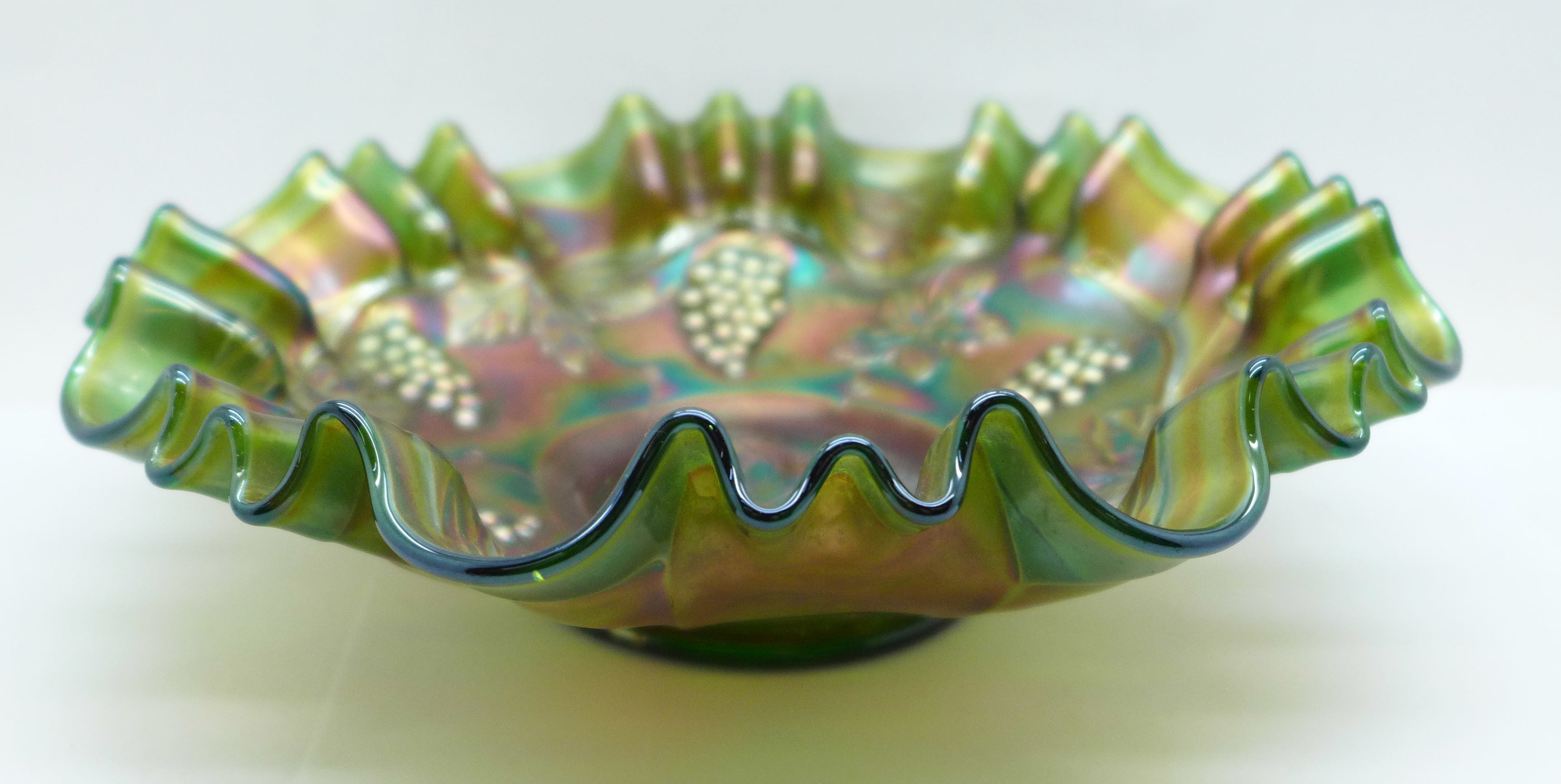 A green carnival glass dish with wavy edge and grape design, 21.5cm