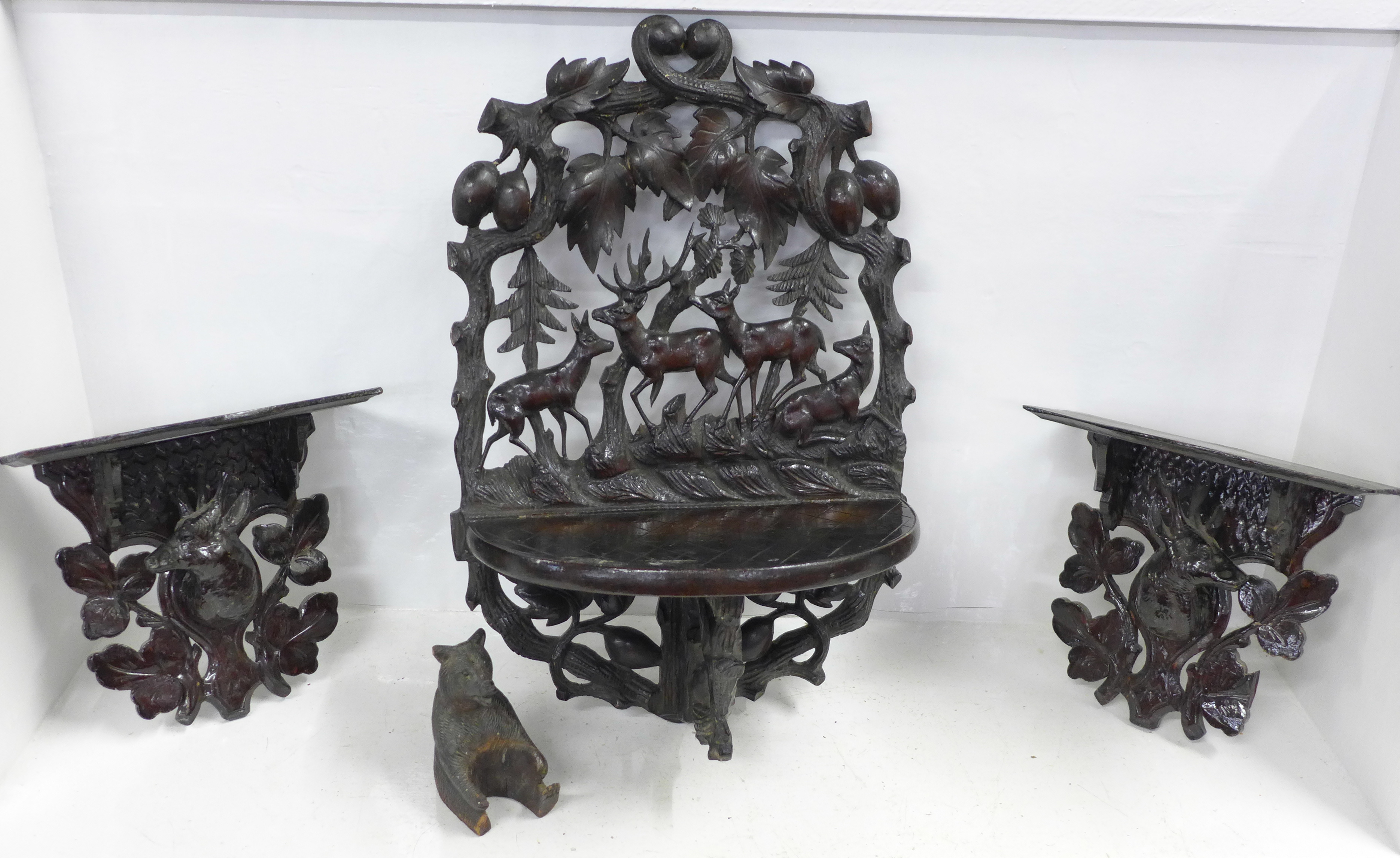 A Black Forest carved seated bear and three carved shelves