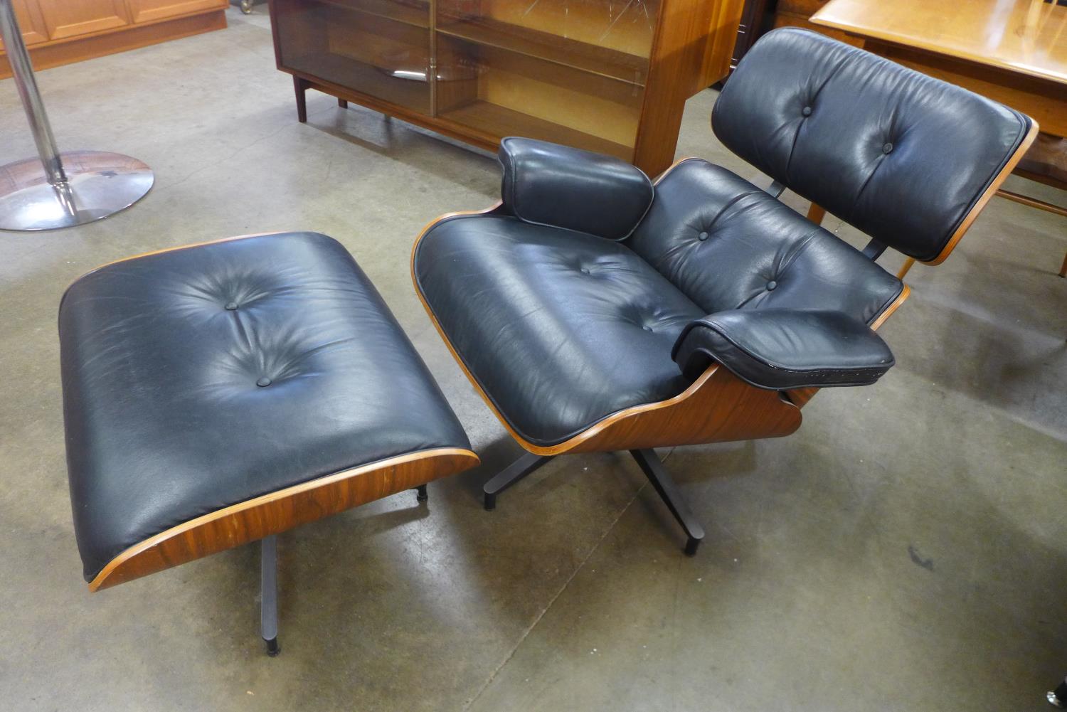 A Charles & Ray Eames style black leather, walnut and chrome revolving lounge chair and stool