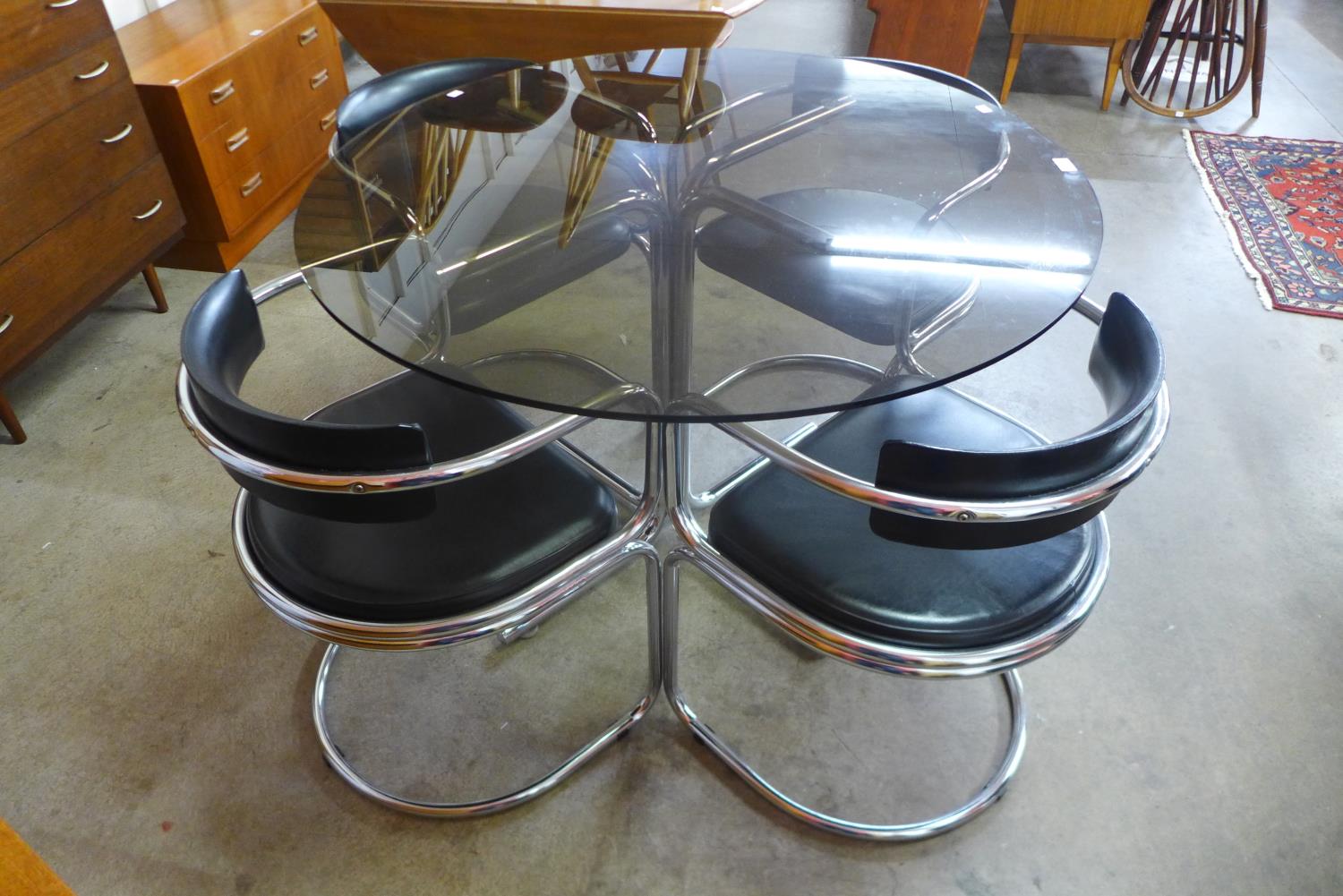 A chrome and glass topped circular table and four chairs