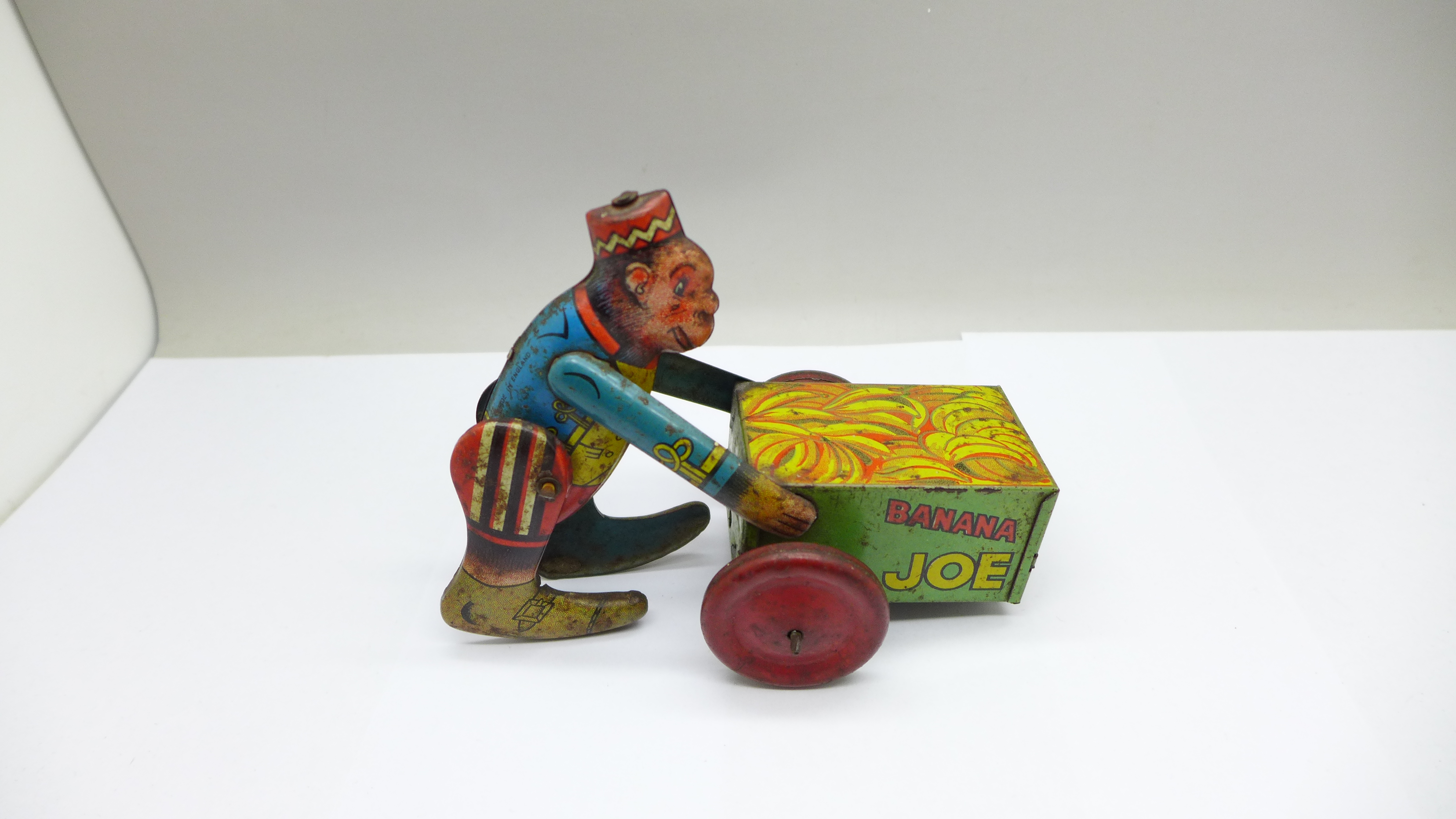 A vintage tin-plate clockwork toy monkey on a cart, marked made in England