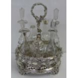 A silver plated seven bottle cruet and stand, adorned with vine leaves, one bottle lacking top