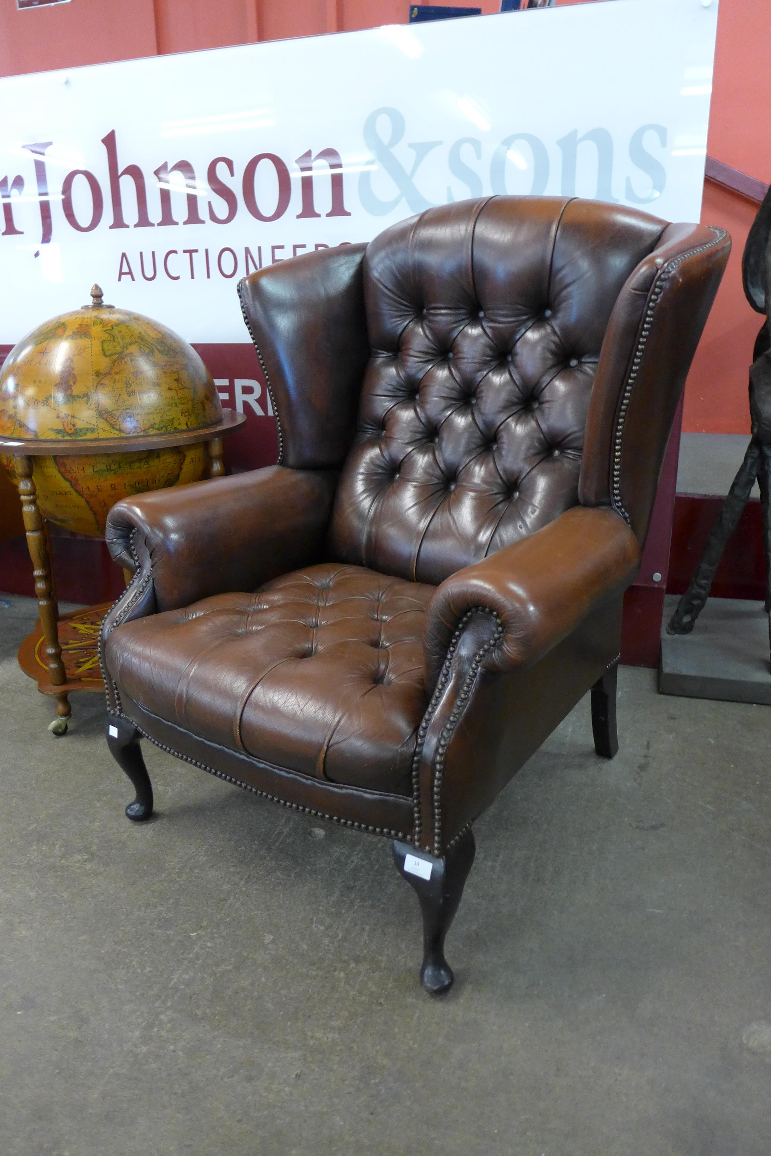 A chestnut mahogany and brown buttoned leather wingback armchair