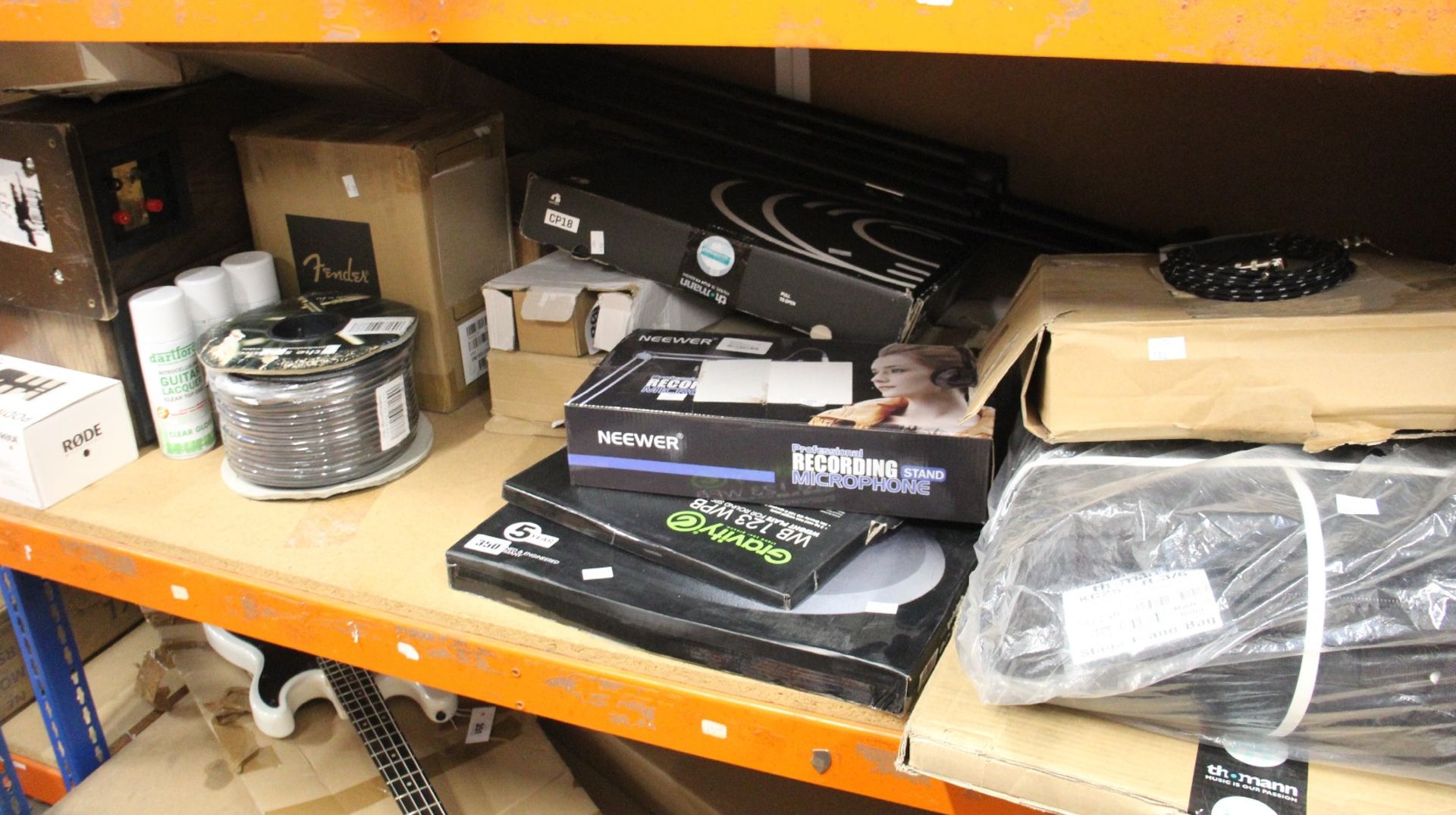 A shelf of miscellaneous music equipment and related items to include a Rode PodMic, a Thomann stage