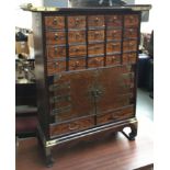 A Chinese hardwood and brass medicine cabinet comprising 20 small drawers, over cupboard and a