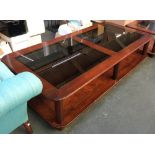 A very large modern hardwood coffee table, the top inset with two square smoked glass panels, with