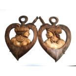 A pair of carved wooden tribal wall plaques, depicting a couple within heart shaped surrounds,