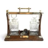 An oak and silver plated tantalus, with two square cut glass decanters and key