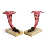 A pair of cranberry glass cornucopias with brass hand terminals, with painted foliate decoration,