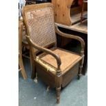 A commode chair, with caned back and hinged seat, in need of some restoration