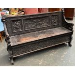 An oak settle, heavily carved with Medieval scenes, the arms carved as sea monsters, hinged seat