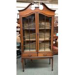 A mahogany glazed display cabinet, broken swan neck pediment over two glazed doors opening to reveal