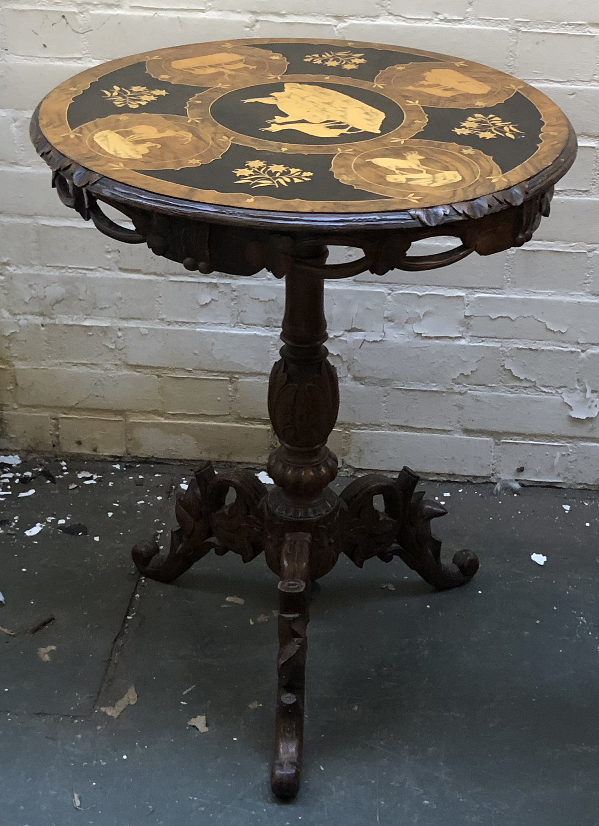 A circular marquetry occasional table, depicting impala, stags and other horned beasts, on a