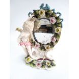 A 19th century porcelain model depicting a cherub looking into an encrusted mirror, 22cmH, marked to