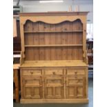 A pine kitchen dresser, the top with shaped apron, over two shelves, on a base of three drawers