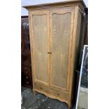 A light oak hanging wardrobe, pediment top over two cupboard doors, with single drawer below,