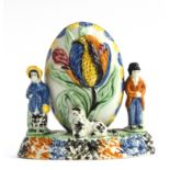 An unusual Staffordshire Prattware moneybox, decorated with figures and a dog beside an oval