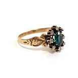 A gold and emerald ring set with 7 diamonds (one missing), marks rubbed but tests as 9ct, size N,