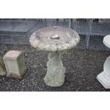 A stoneware bird bath on dolphin entwined column