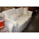 A cream two seater settee with lose covers and cus