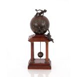 A mahogany and spelter mantel clock, in the form of a sphere with cherub surmounts raised on a