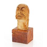 A primitive stone head carving, set to a wooden block plinth, 28cm high