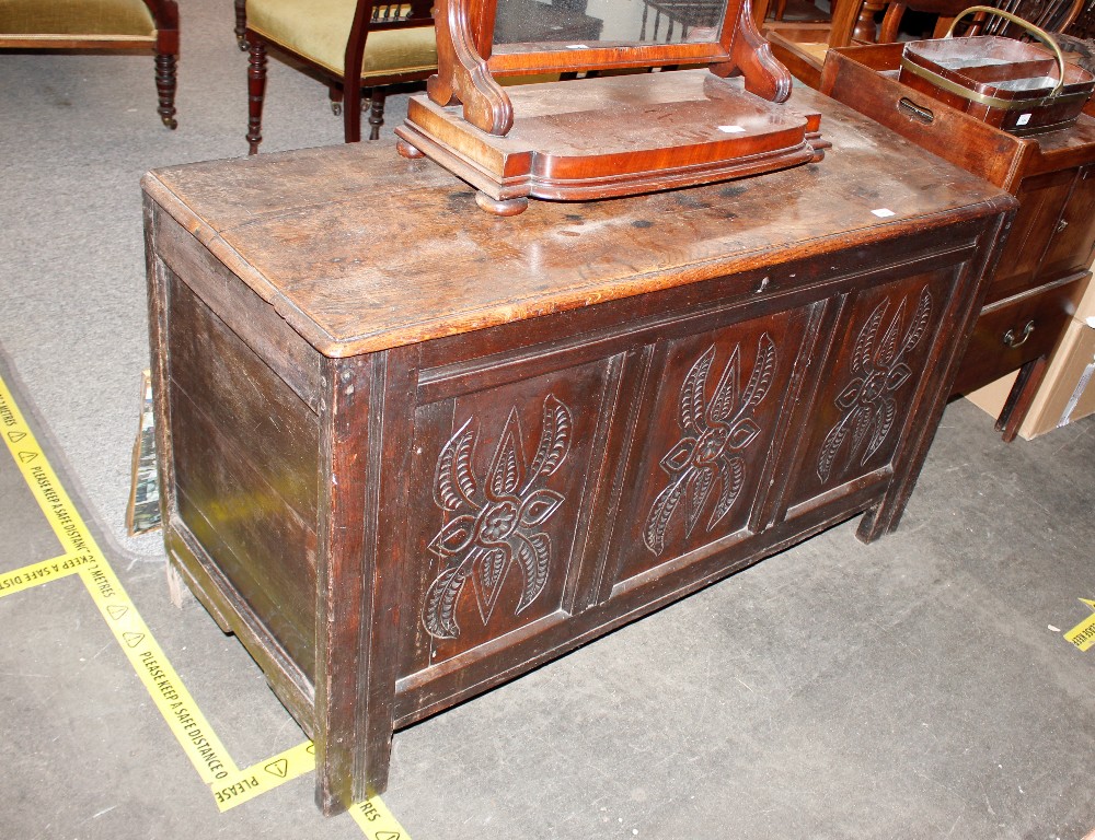 An antique oak coffer, having triple panelled carved front raised on square section supports,