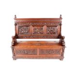 A heavily carved Flemish style settle, the back with triple panels decorated with tavern figures,