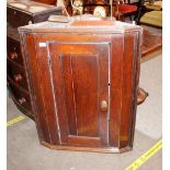 An antique oak hanging corner cupboard, the interior shelves enclosed by a single panelled door,