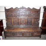 An antique carved oak settle, the detachable shaped panelled back profusely decorated with beasts