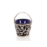 A white metal sugar pail, with pierced foliate decoration, swing handle and blue glass liner, 10cm