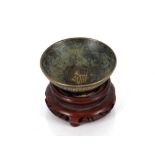 A small oriental bronze dish, having Greek key decoration on a carved base, 6cm dia.