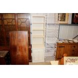 A narrow cream painted bookcase with drawer and cu