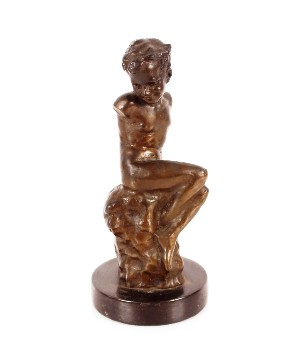 An abstract bronze figure of a boy seated on a roc