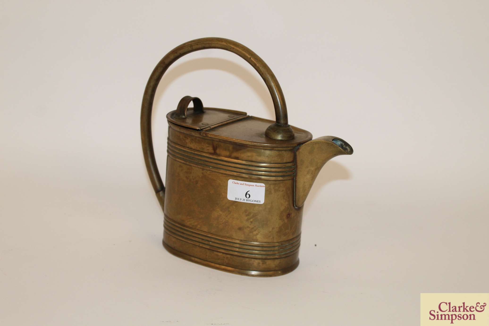 An antique brass watering can with loop handle