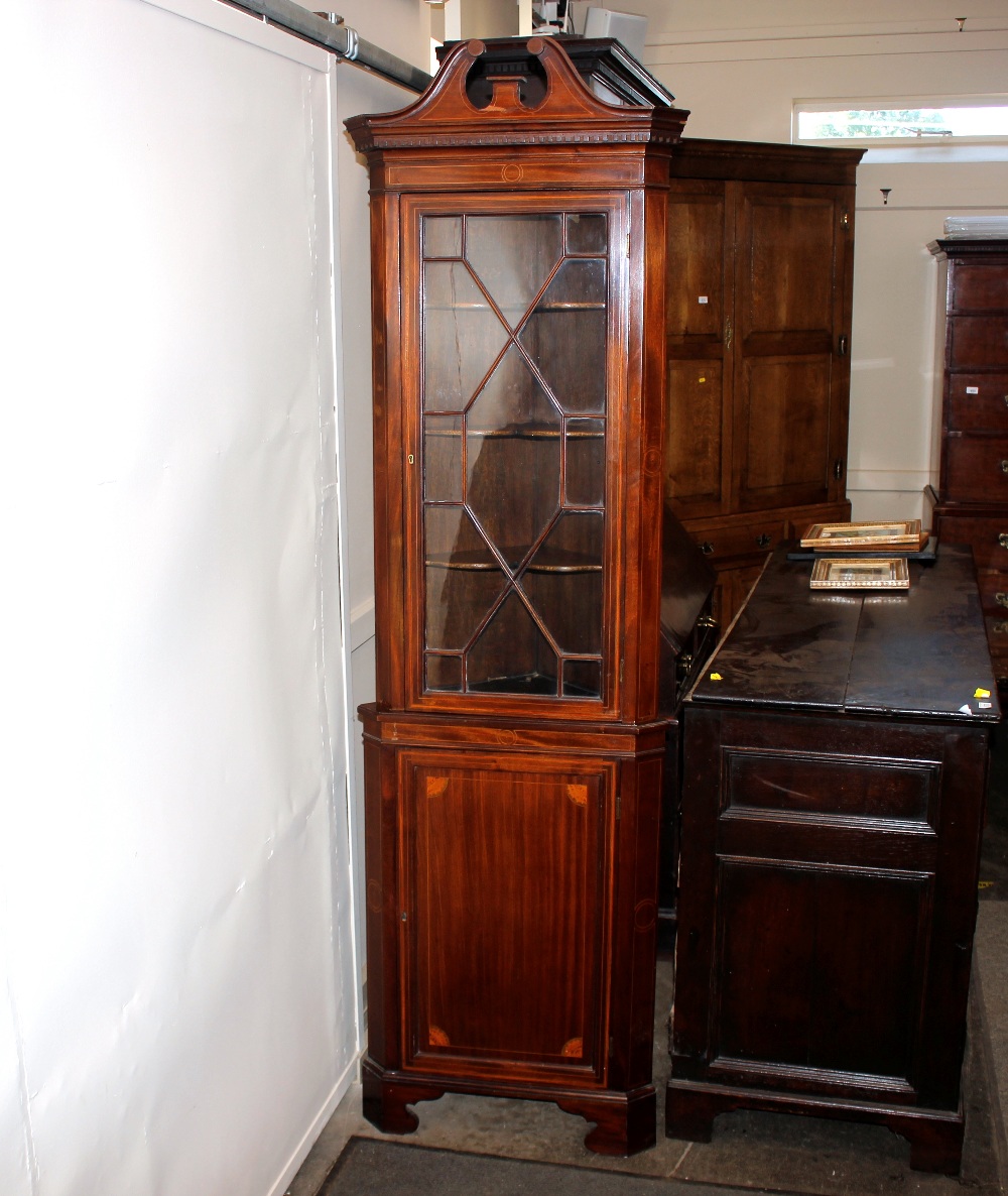 An Edwardian inlaid mahogany corner cupboard, the upper shaped shelves enclosed by a glazed panelled