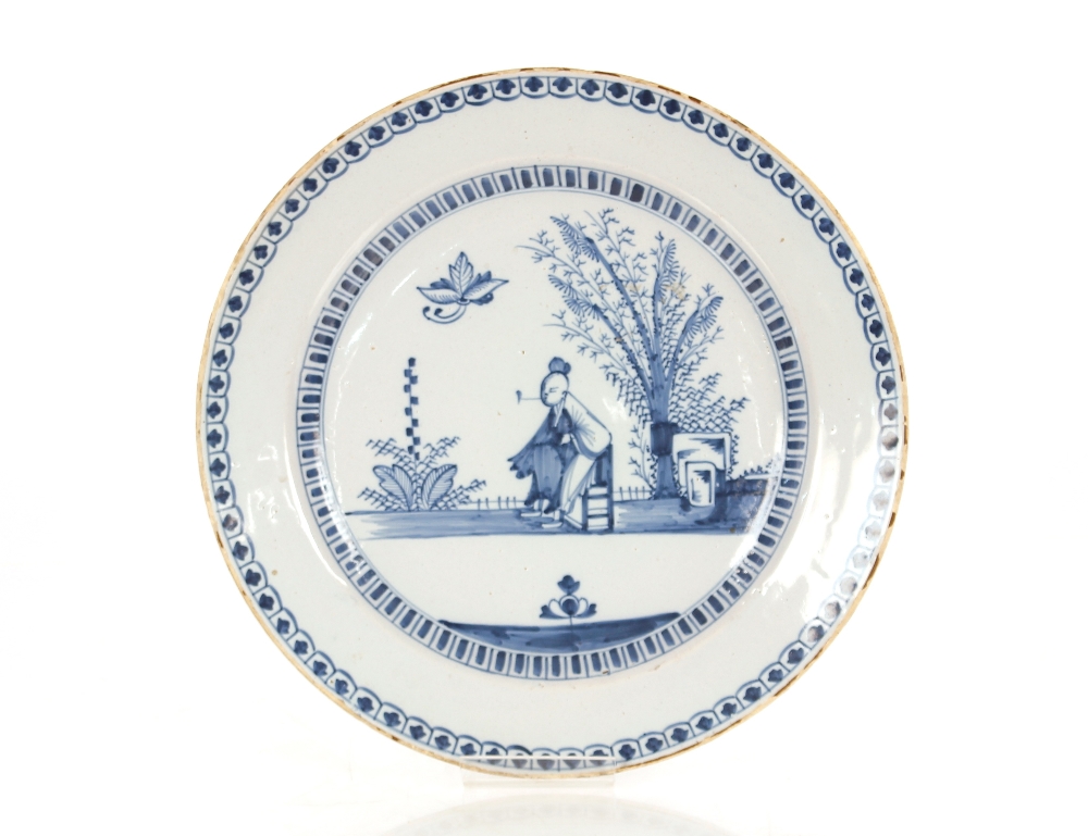 An 18th Century English Delftware blue and white charger, painted with an Oriental figure smoking