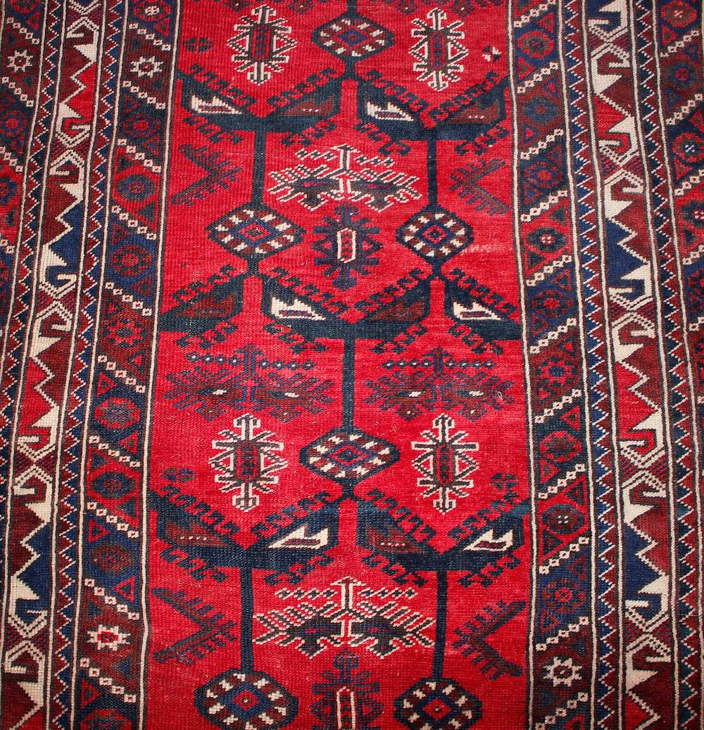 A Middle Eastern wool rug, of Caucasian design having stylised motifs on a brick red ground, 186cm x